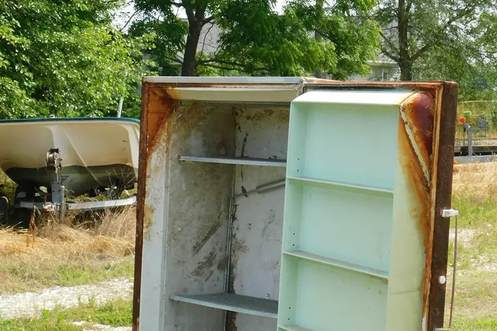 An old rusted refrigerator with its door open, awaiting disposal