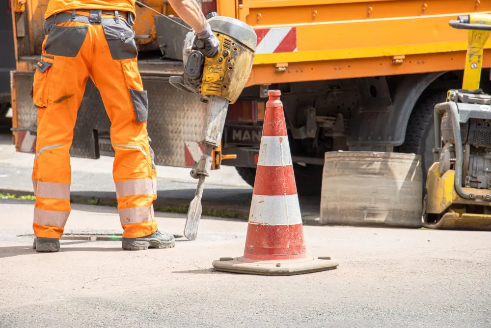 A worker breaking up pavement with a jackhammer beside a work truck