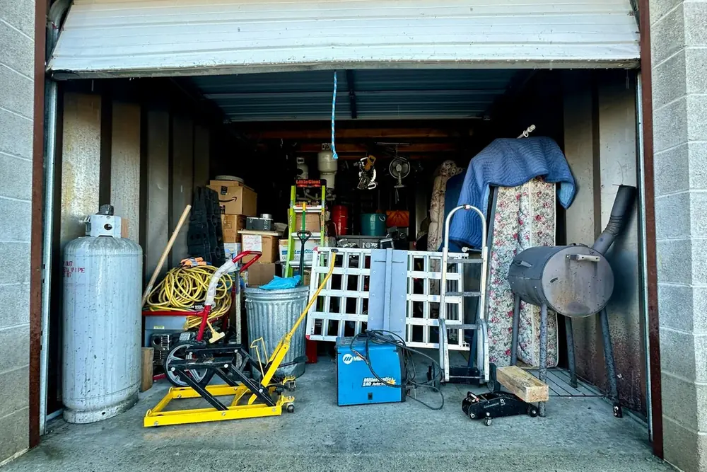 A garage packed floor to ceiling with tools, boxes, a mattress and household clutter