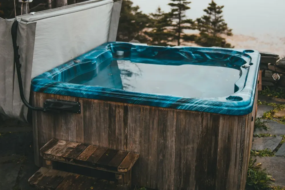 An old outdoor hot tub with a weathered wooden cabinet, cover folded back