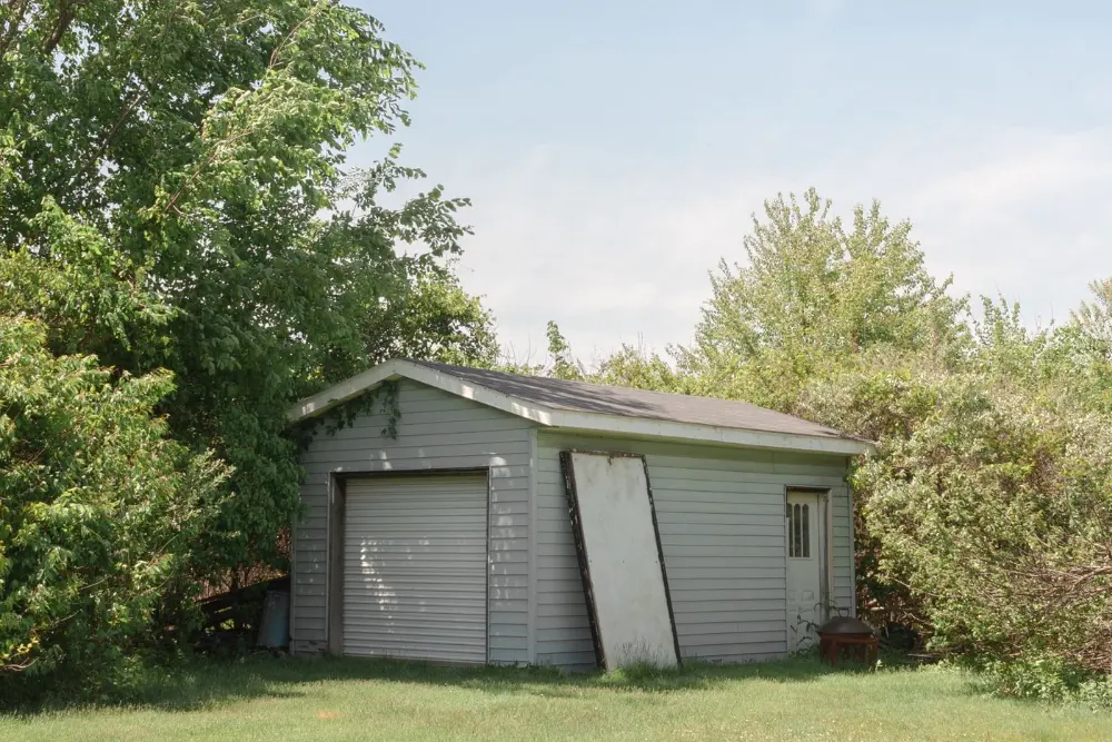 A weathered backyard shed with a broken door leaning against it
